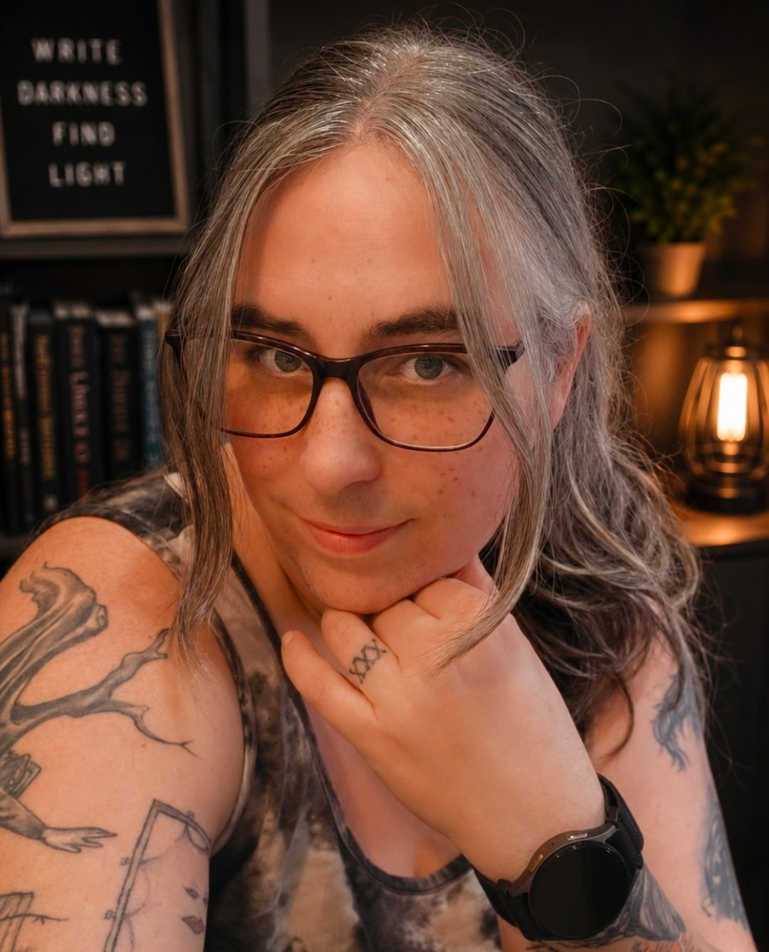 Portrait of author S. B. Collins smiling, chin resting on her hand, in front of a bookshelf